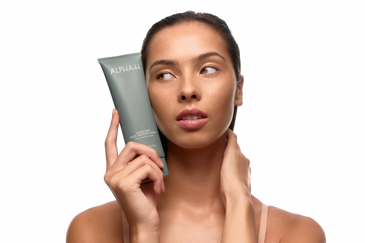 Alpha-H Clear Skin Face & Body Wash modèle avec le tube près du visage