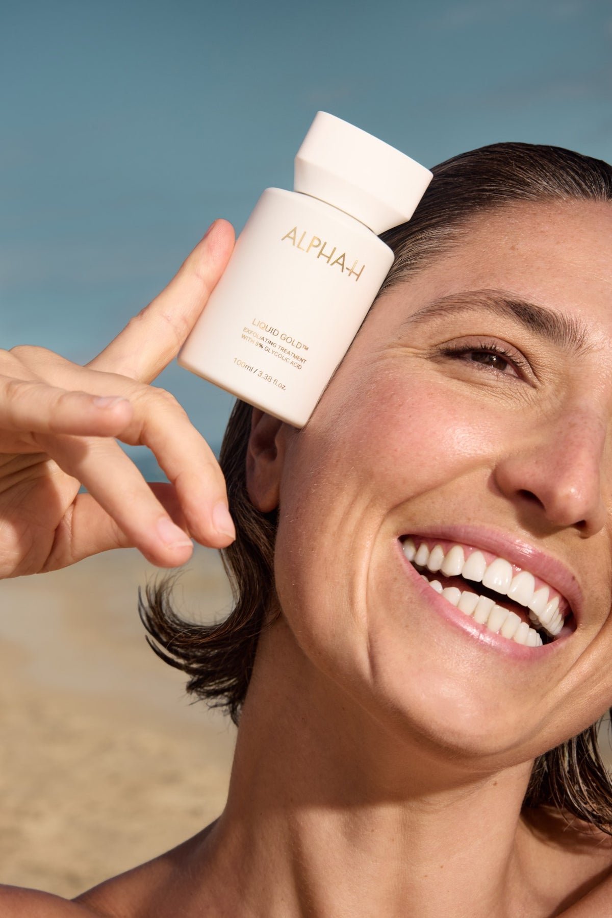 Alpha-H Liquid Gold Exfoliating Treatment modèle avec le flacon au bord de la mer