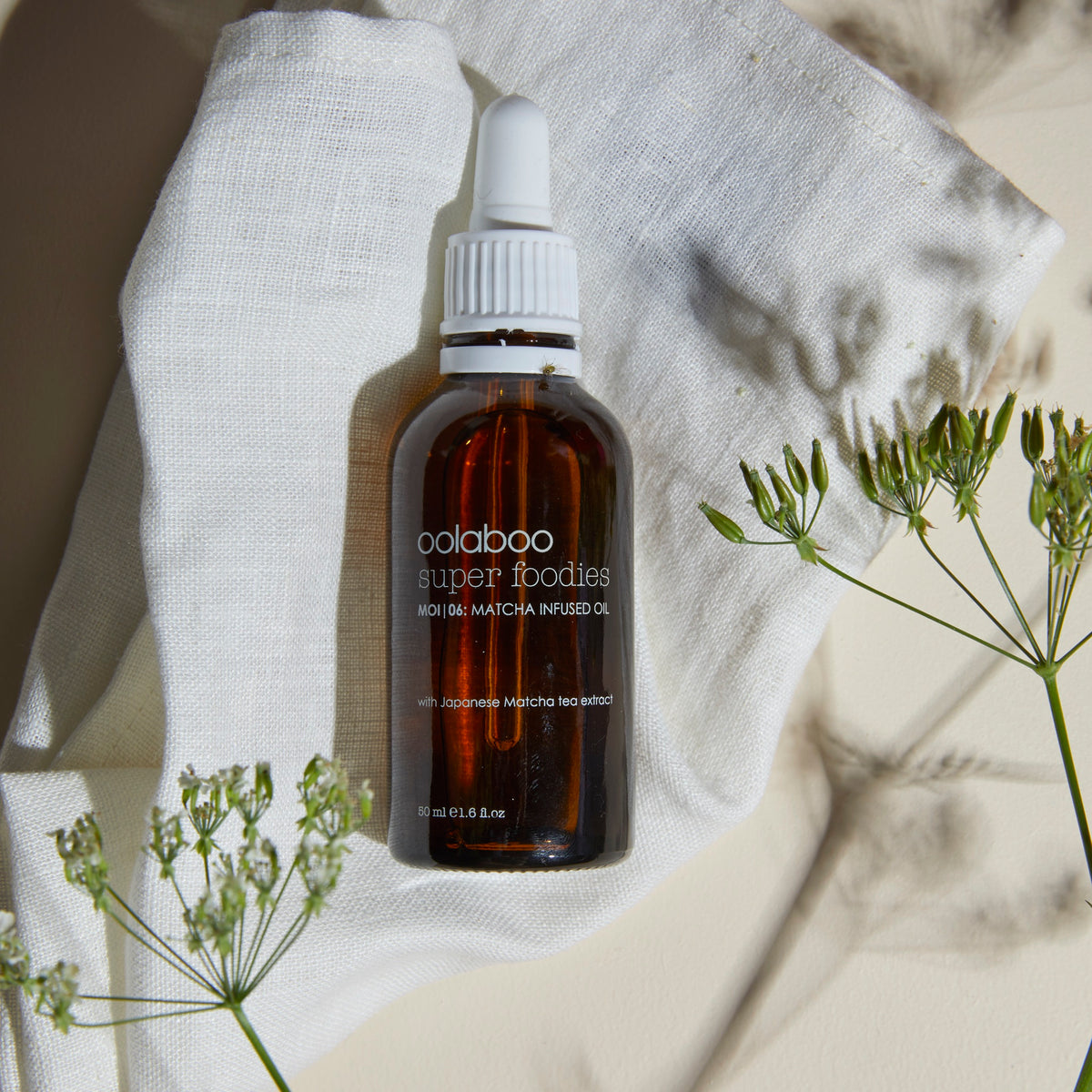 Oolaboo Super Foodies Matcha Infused Oil sur un linge de lin avec des fleurs