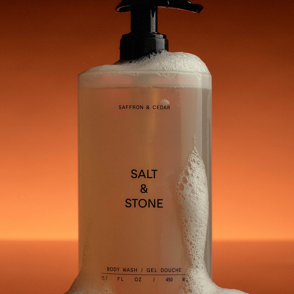 Salt & Stone Body Wash Saffron & Cedar flacon met schuim in oranje licht